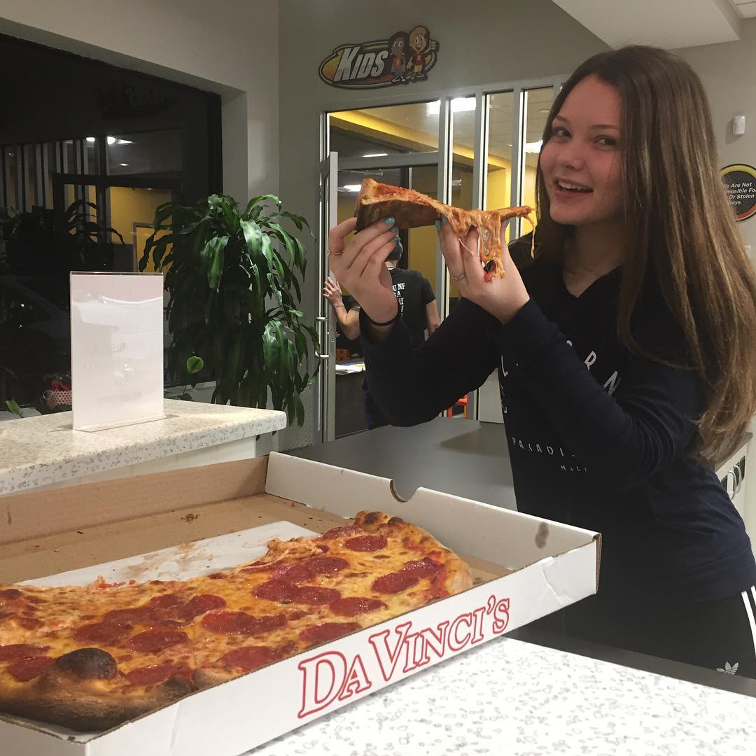 Customer holding a pizza slice beside a Da Vinci's pizza box